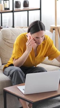 Evde dizüstü bilgisayar ve belgelerle çalışırken uzaktan danışmanlık hizmeti veren tatmin olmuş bir kadın, görevleri verimli bir şekilde dengeliyor. Dikey video.