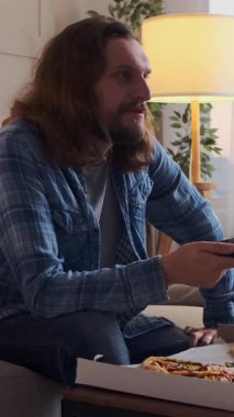 Televizyon seyreden, pizza yiyen ve evde boş vakitlerde bira içen rahat ve eğlenceli bir akşamın tadını çıkaran tatmin olmuş bir adam. Dikey video.