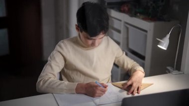 Bir evin masasında, grafik kağıdına geometrik şekiller çizen bir gencin yan görüntüsü..