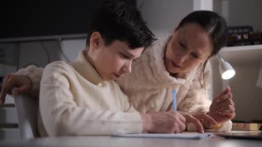 Bir annenin, genç oğlunun üzerine eğildiği ana yakın görüş. O, evde geometri çizerken..