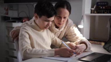 Ergen oğluna rehberlik eden bir annenin yan görüntüsü. Ev masasında elinde lambayla ödev yazarken..