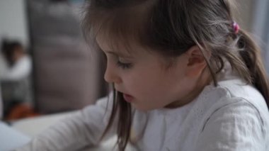 Yatak odasındaki bir masada renkli kalemlerle resim çizen genç bir kızın yakın portresi..