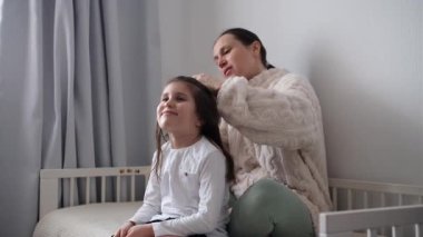 Yetişkin bir kadının yatak odasında saç fırçasıyla genç bir kızın saçını taramasının yan görüntüsü..