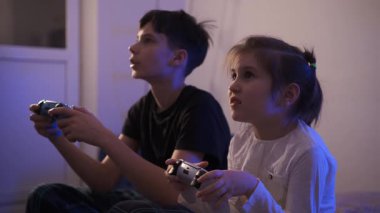 Oyun kontrolörlerini elinde tutan ve akşamları evde birlikte konsol oynayan genç bir kız ve erkek çocuğu yakından görülüyor..