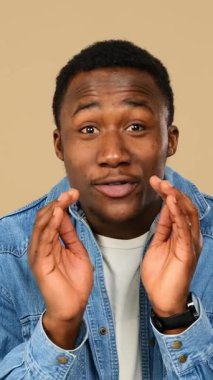 Yetişkin bir adam, bej arka planda dudaklarında parmaklarıyla el sallıyor..