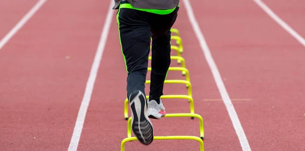 在田径运动训练中 一名高中跑步者在跑道上跑过黄色迷你栏的后视镜 — 图库照片