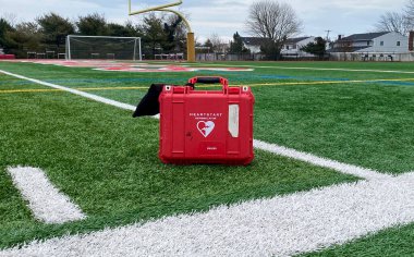 West Islip, New York, ABD - 3 Ocak 2023: Bir defibrilatör makinesi, kırmızı bir çantada yeşil bir futbol sahasında duruyor.