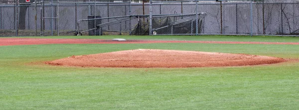 An empty turf baseball field looking over the pitchers mound to first base.