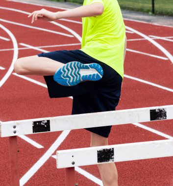 Rear view of a high school hurdle runner performing sports drills on a red track at practice.