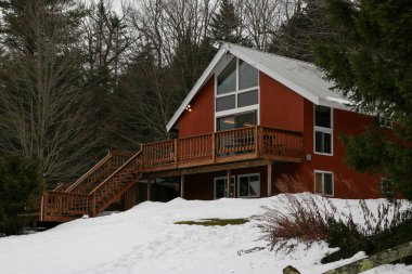 A classic A-Frame Ski vacation home with a wood deck and staircase with snow on the ground.