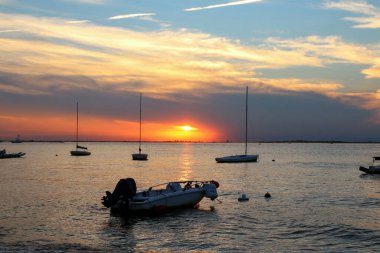 Güneş arka planda motorlu ve yelkenli teknelerle batıyor. Büyük indirimli Long Island Körfezi üzerinden Fire Island 'dan batıya bakıyor..