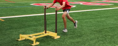 One runner pushing a yellow sled on a turf field during summer preseason camp.