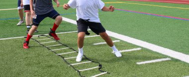 Young football athletes running in the ladder drill on a turf field during summer training camp.
