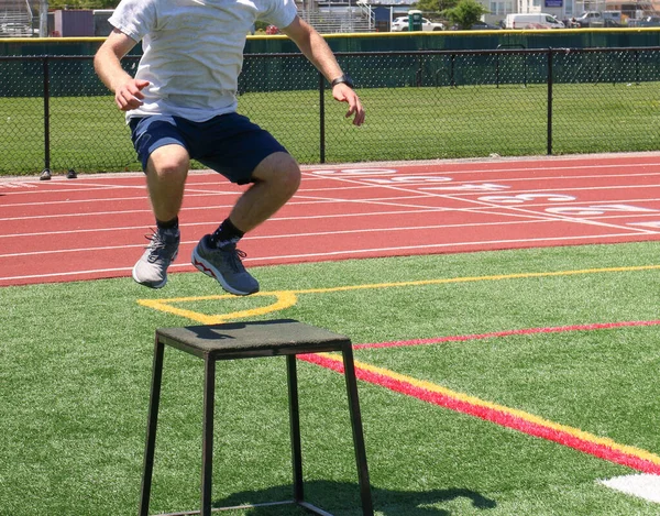 High school boy in the air over a plyos box exercising on a turf field during summer sports camp.