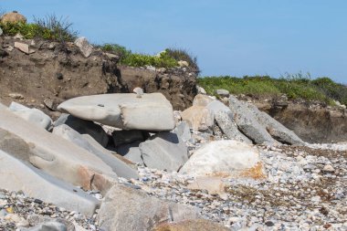 Large boulder on a beach in Narragansett Rhode Island in front of very eroded shoreline.