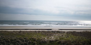 İnsansız hava aracı sahilin kum tepelerinde süzülür sakin ve bulutlu bir kış gününde Atlantik Okyanusu 'nu seyreder..