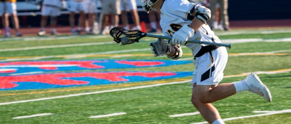 High school lacrosse player running down the field with the ball during a game.