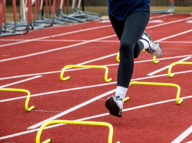 Siyah tayt giymiş bir koşucu bacakları antrenman sırasında şeritte 15 santimlik sarı muz engellerini aşıyor.. 