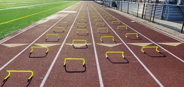 Four rows of yellow six inch mini hurdles set up in lanes on a track for runners to run over performing the wicket drill.