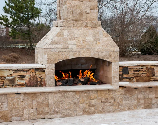 A gas fireplace made from paving stone burning outside on a patio close up.