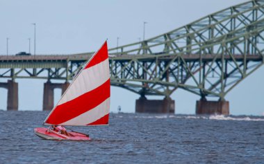 Close up of one red and white sunfish sailboat sailing on the Great South Bay close to the bridge catching some wind.