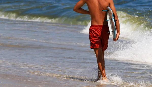 在长岛吉尔戈海滩 一名年轻男子背着冲浪板 身穿红色浴衣 在水边行走的背影 — 图库照片