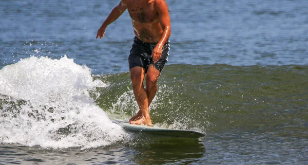 在一个阳光明媚的海滩上 一个没有汗衫的男人一边走着 一边跨上他的滑板 一边在海浪中冲浪 — 图库照片