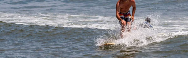 一个男人穿着五颜六色的游泳衣 穿着左边没有复制空间的衬衫 在一个小浪上冲浪和飞溅 — 图库照片