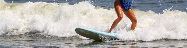 骑在靠岸的蓝色冲浪板上的一个年轻姑娘的腿在她的旅程快结束的时候靠得很近 — 图库照片