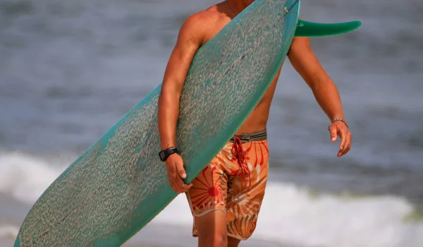 サーファーは ぼやけた背景を持つビーチの岸に彼のサーボを運ぶ — ストック写真