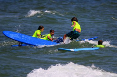 Gilgo Beach, New York, ABD - 25 Temmuz 2023: Long Island 'daki Bunger Sörf Kampı' nda sörf yaparken neon yeşil tişörtlü çocuklar.