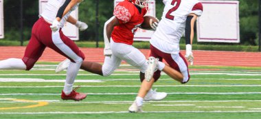 Lise futbolu bir maç sırasında savunmacılardan kaçarak koşuyor.