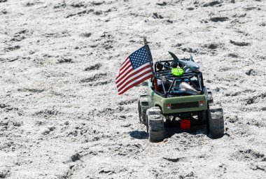 Üstünde Amerikan bayrağı olan bir oyuncak kamyon kumsalda kumsalda sürüyor.