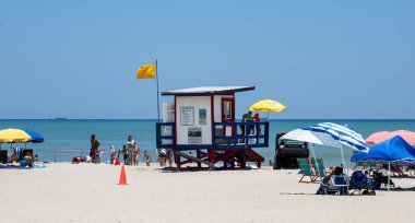 Cocoa Beach, Florida, ABD - 27 Haziran 2023: Sahilde şemsiyeli kırmızı, mavi ve beyaz bir cankurtaran durağı ve Florida Cocoa Beach 'te sarı bir bayrak