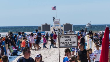 Jones Beach, Wantagh, ABD - 24 Mayıs 2019: Kumlu bir plajın tepesinde duran bir kalabalık kumsalın üzerinde mavi bir minder üzerinde cankurtaran istasyonuna doğru yürüyor