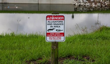 A sign warning of alligators and snakes in area by a stream in Florida USA