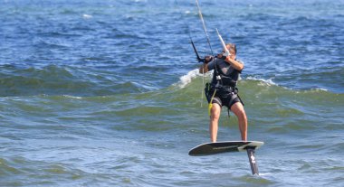 Gilgo Beach, New York, ABD - 13 Ağustos 2023: New York kıyılarında Atlantik Okyanusu 'nda sörf yaparken uçurtma tutan bir adamın yan görüntüsü.