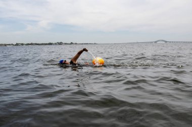 Körfezde yüzen bir kadın, arka planda New York 'taki Great South Bay Köprüsü olan turuncu bir şamandıra giyiyor..