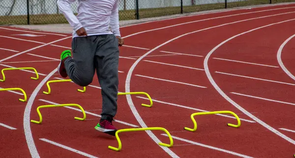 stock image Front view of a high school boy running over small yellow mini hurdles during track practice.