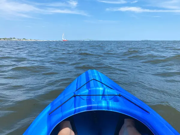 Uzakta bir köprüsü olan sakin, berrak bir mavi körfezde bir kişi kano kullanıyor. Gökyüzü parlak bir mavi ve güneş parlıyor..