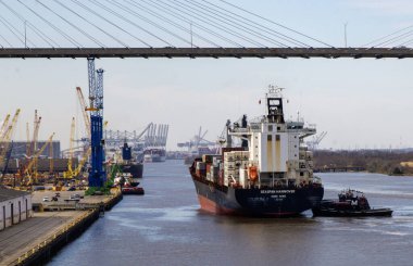 Savannha, Georgia, USA - 21 February 2024: A Cargo Ship with containers stacked on top of each other going under a bridge in the Savannha River. clipart