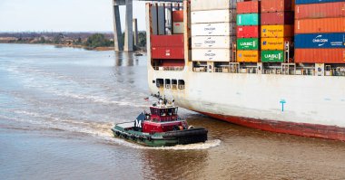 Savannha, Georgia, USA - 21 February 2024: A Cargo Ship with containers stacked on top of each other Journeying Through the Savannha River with a tug boat escort. clipart