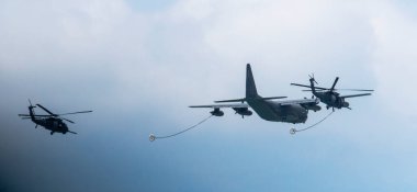 Jones Beach, New York, ABD - 29 Mayıs 2022: Biri önde diğeri arkada olmak üzere iki helikopterli büyük bir askeri kargo uçağı dizilimde uçuyor. 