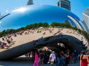 Şikago, Illinois, ABD - 18 Temmuz 2024: Cloud Gate olarak bilinen büyük, parlak, yansıtıcı bir heykel, ziyaretçilerin etrafında toplandığı aşağıdan izleniyor. Heykel, çevresindeki şehrin ufuk çizgisini yansıtıyor ve çarpık bir görüntü yaratıyor.. 
