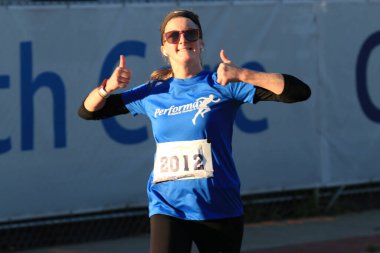 West Islip, New York, ABD - 22 Ekim 2023: Bir bayan koşucu Long Island 'da bir maratonda koşarken fotoğrafçıya başparmak sallıyor ve gülümsüyor.