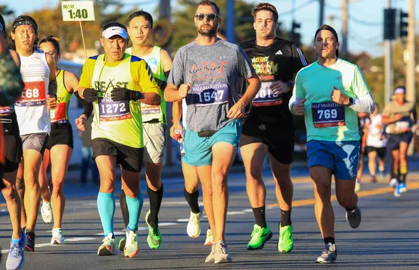 stock image West Islip, New York, USA - 22 October 2023: Front view of a pacesetter running with a group of runners during a half marathon pacing them to a goal time of 1:40.