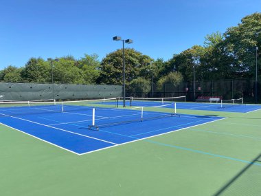 Dört portatif Pickleball ağı iki mavi ve yeşil tenis kortuna yerleştirildi. Mükemmel bir günde gökyüzü maviyken dört tane Pickleball sahası yapmak için..