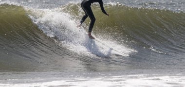 Man at the beginning of catching a wave while surfing in the Atlantic Ocean wearing a full black wetsuit. clipart