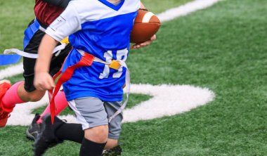 Close up of a young flag football player running with the ball during a youth flag football game. clipart