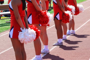 Bir futbol maçında ponponlarını arkalarında tutan lise ponpon kızlarının arka plandaki görüntüsü.